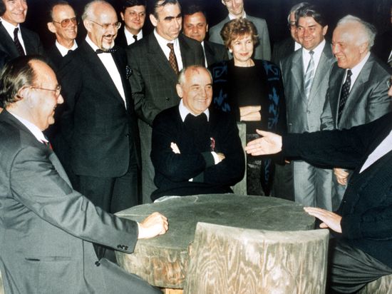 ARCHIV - Bundeskanzler Helmut Kohl (r), der sowjetische Staatspräsident Michail Gorbatschow (M), Bundesaußenminister Hans-Dietrich Genscher (l) und der sowjetische Außenminister Edward Schewardnadse (2.v.r.) unterhalten sich am 15.07.1990 an einem rustikalen Arbeitstisch in Archys, Russland. Im Hintergrund rechts von Gorbatschow steht seine Frau Raissa. Bei diesem Treffen im Kaukasus soll die Deutsche Einheit ausgehandelt worden sein. Foto: dpa ++ +++ dpa-Bildfunk +++