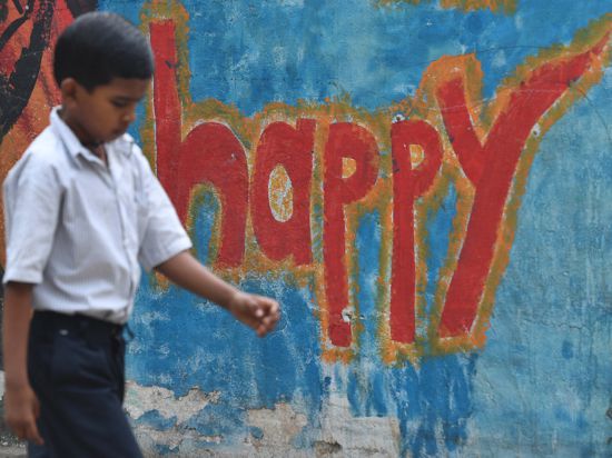 Ein indischer Junge steht vor einer Hauswand mit einem Graffiti.