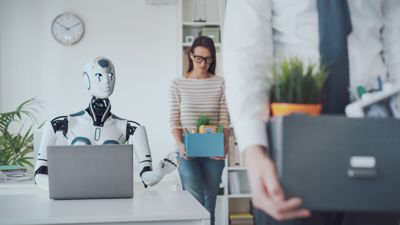 Ein Roboter sitzt am Computer – und zwei menschliche Arbeitnehmer verlassen mit gesenktem Haupt das Büro. Ihre Habe tragen sie in kleinen Kisten davon. 