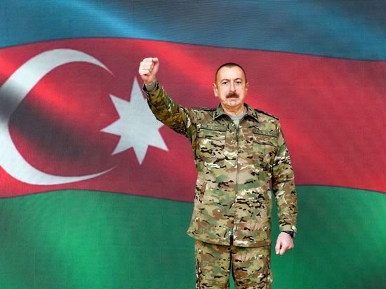 Ilham Aliyev, Präsident von Aserbaidschan, steht in Baku vor einer Projektion der Nationalflagge.