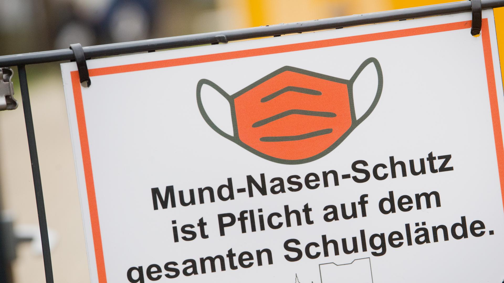 Der Schriftzug «Mund-Nasen-Schutz ist Pflicht auf dem gesamten Schulgelände» und ein Piktogramm einer Maske sind auf einem Schild am Eingang einer Schule zu sehen.
