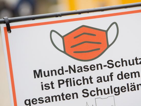 Der Schriftzug «Mund-Nasen-Schutz ist Pflicht auf dem gesamten Schulgelände» und ein Piktogramm einer Maske sind auf einem Schild am Eingang einer Schule zu sehen.