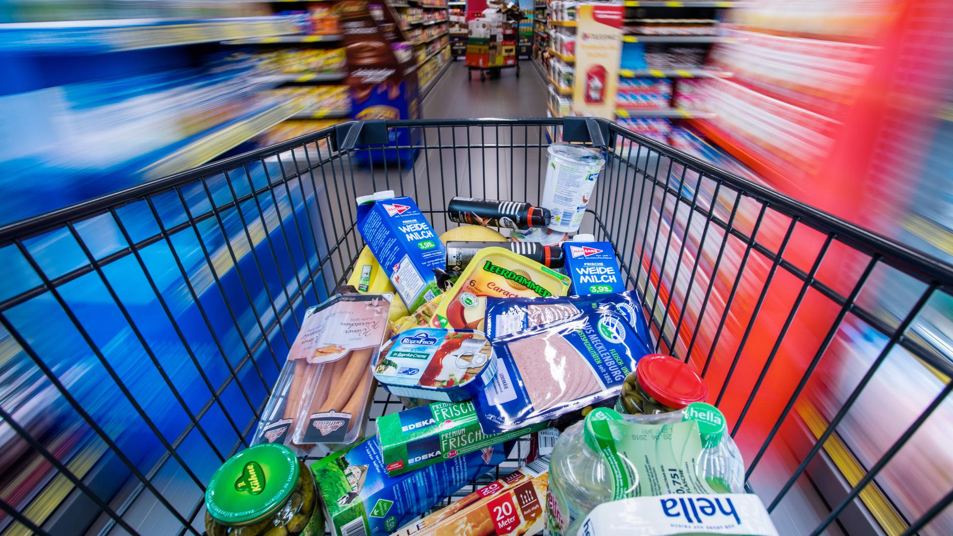  Ein Einkaufswagen mit Lebensmitteln wird durch die Regalreihen in einem Supermarkt geschoben. 