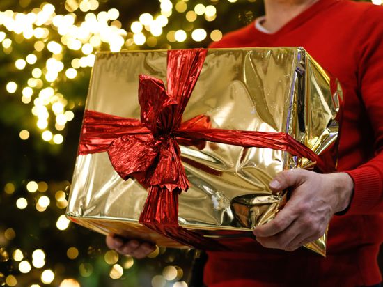 ARCHIV - 13.12.2018, Berlin: ILLUSTRATION - Ein Mann hält ein golden eingepacktes Weihnachtsgeschenk in den Händen. Im Hintergrund ist ein Weihnachtsbaum zu sehen. Foto: Gerald Matzka/dpa-Zentralbild/dpa +++ dpa-Bildfunk +++