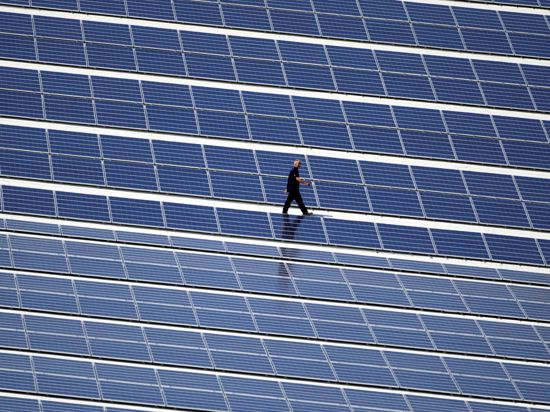 Ein Techniker geht über ein Dach, auf dem eine Photovoltaik-Anlage montiert wurde. 