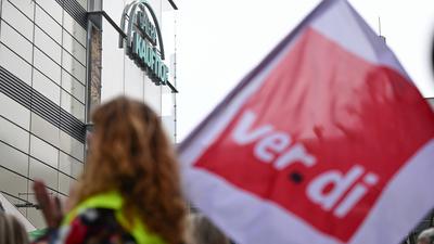 Beschäftigte protestieren mit einer Fahne der Gewerkschaft Verdi vor einer Filiale von Galeria Karstadt Kaufhof.