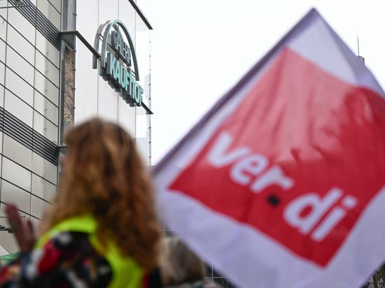 Beschäftigte protestieren mit einer Fahne der Gewerkschaft Verdi vor einer Filiale von Galeria Karstadt Kaufhof.