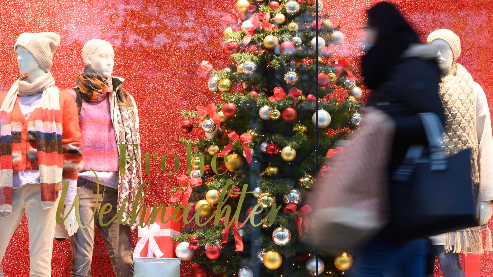 Eine Passantin geht mit einer Papiertüte auf einer Einkaufsstraße Prager Straße vor einem Schaufenster mit der Aufschrift «Frohe Weihnachten» entlang. 