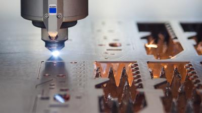 Ein Laser des Maschinenbauers Trumpf GmbH & Co. KG schneidet  in einer Produktionshalle  auf einer Platte. 