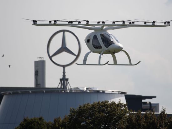 Ein sogenannter Volocopter fliegt neben einem Mercedes-Stern.+++