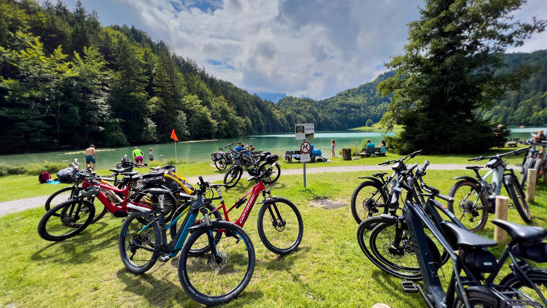 Mountainbiker haben ihre E-Bikes abgestellt und baden in einem See in Füssen.