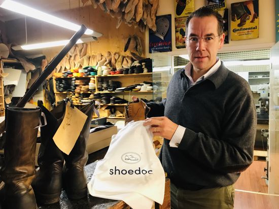 Ein Mann steht in einer Schuhwerkstatt und packt einen reparierten Herrenschuh in einen weißen Beutel