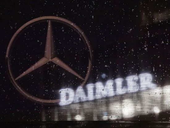 Das Logo der Daimler-AG ist an der Konzernzentrale zu sehen, im Vordergrund ist ein Mercedes-Stern auf einer Flagge abgebildet, die voller Regentropfen ist.