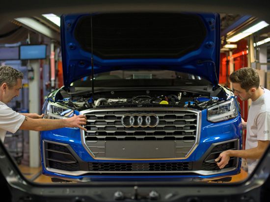 Fertigungsmechaniker bringen an einem Fließband im Audi-Werk die Front an einem Audi an.