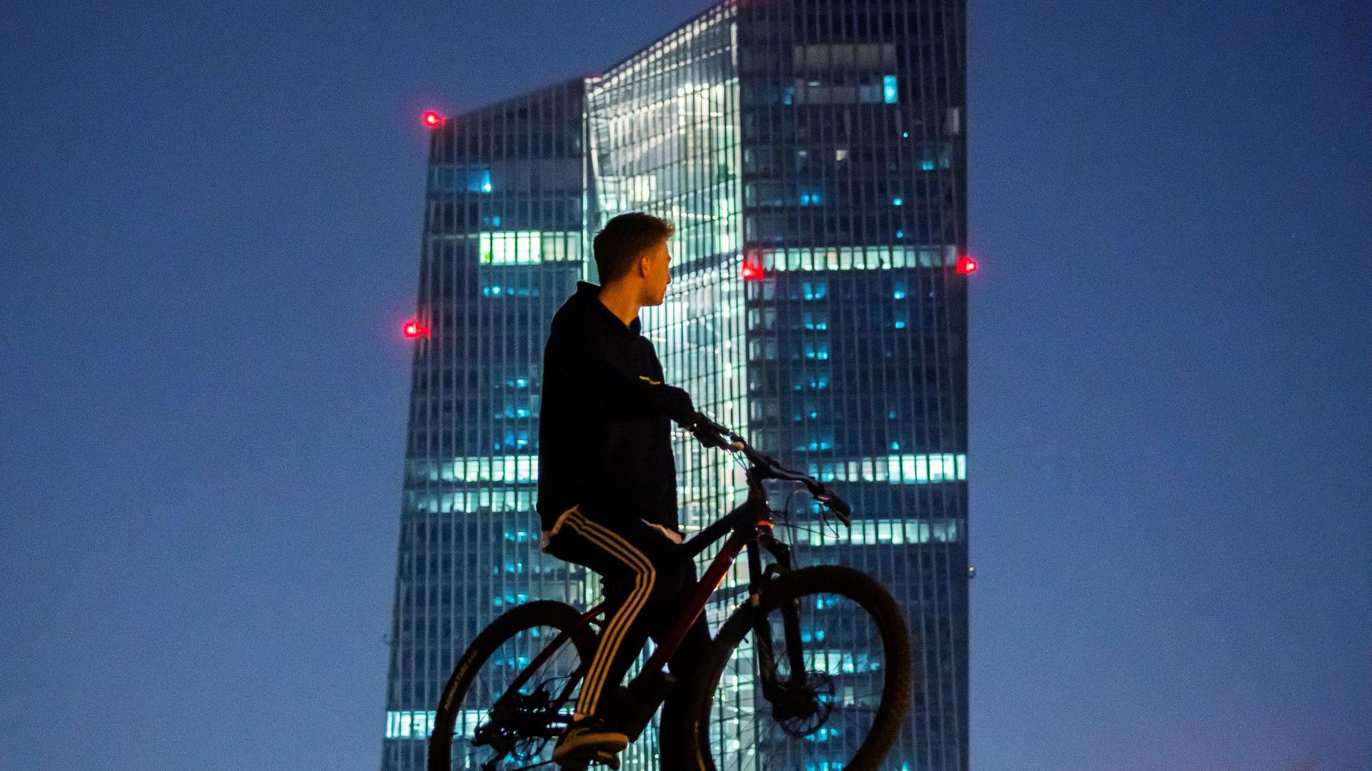 Ein junger Mann steht mit seinem Rad vor dem EZB-Tower. Europas Währungshüter stemmen sich mit Milliarden gegen die beispiellose Konjunkturkrise infolge der Corona-Pandemie.