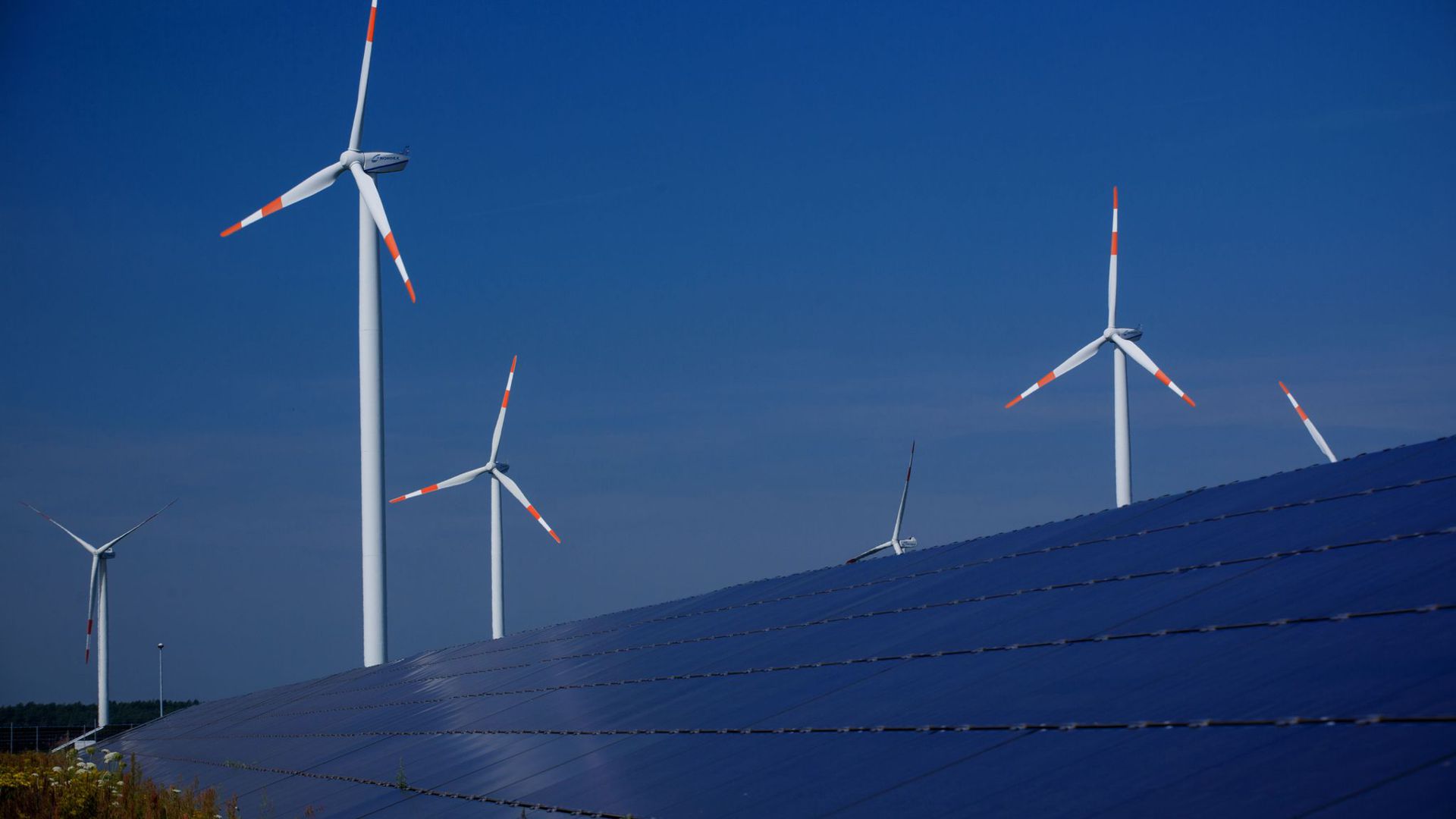 Windräder zur Stromerzeugung drehen sich am hinter einem Solarpark. Der Ökostrom-Anteil soll weiter steigen.