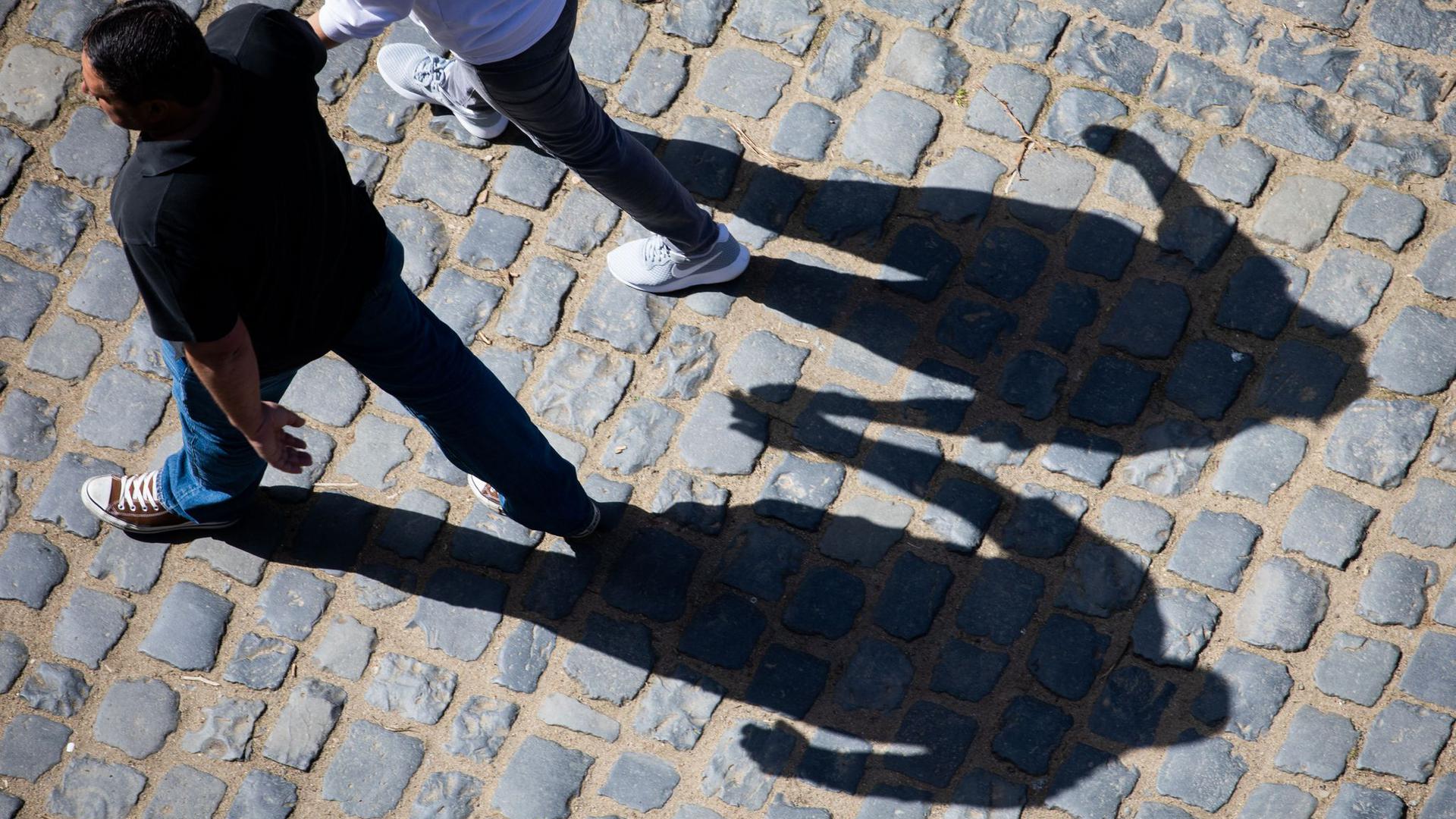 Die Schatten zweier Menschen, die Hand in Hand gehen, zeichnet sich auf dem Pflaster des Schlosses Auerbach ab.