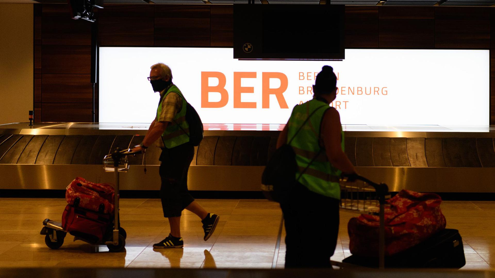 Komparsen in Warnwesten gehen beim Probelauf im Terminal 1 des Hauptstadtflughafens Berlin-Brandenburg (BER) mit ihren Koffern zum Check in.