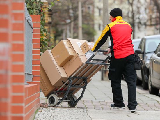 Ein DHL-Paketzusteller geht mit einer Sackkarre voller Pakete zu einem Haus.