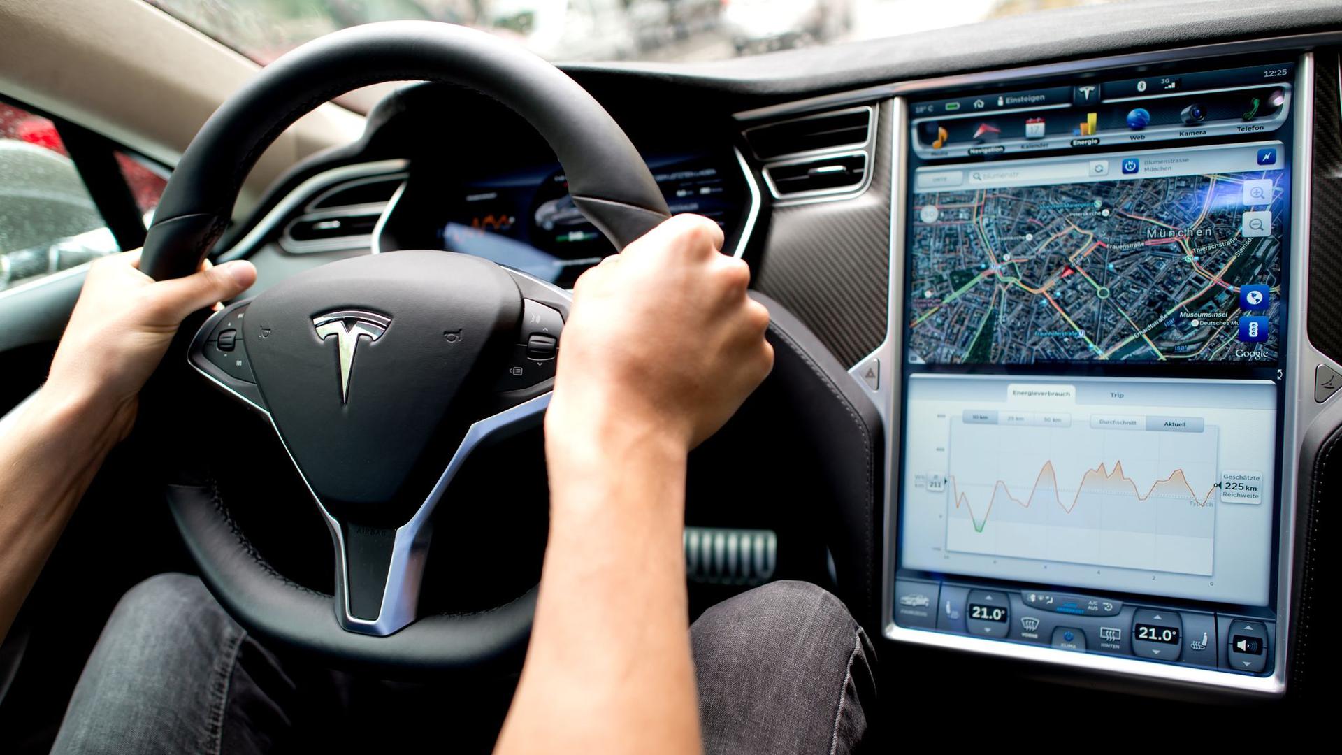 Ein Mann sitzt in einem Tesla Model S am Lenkrad, neben ihm ein großer Monitor im Armaturenbrett.