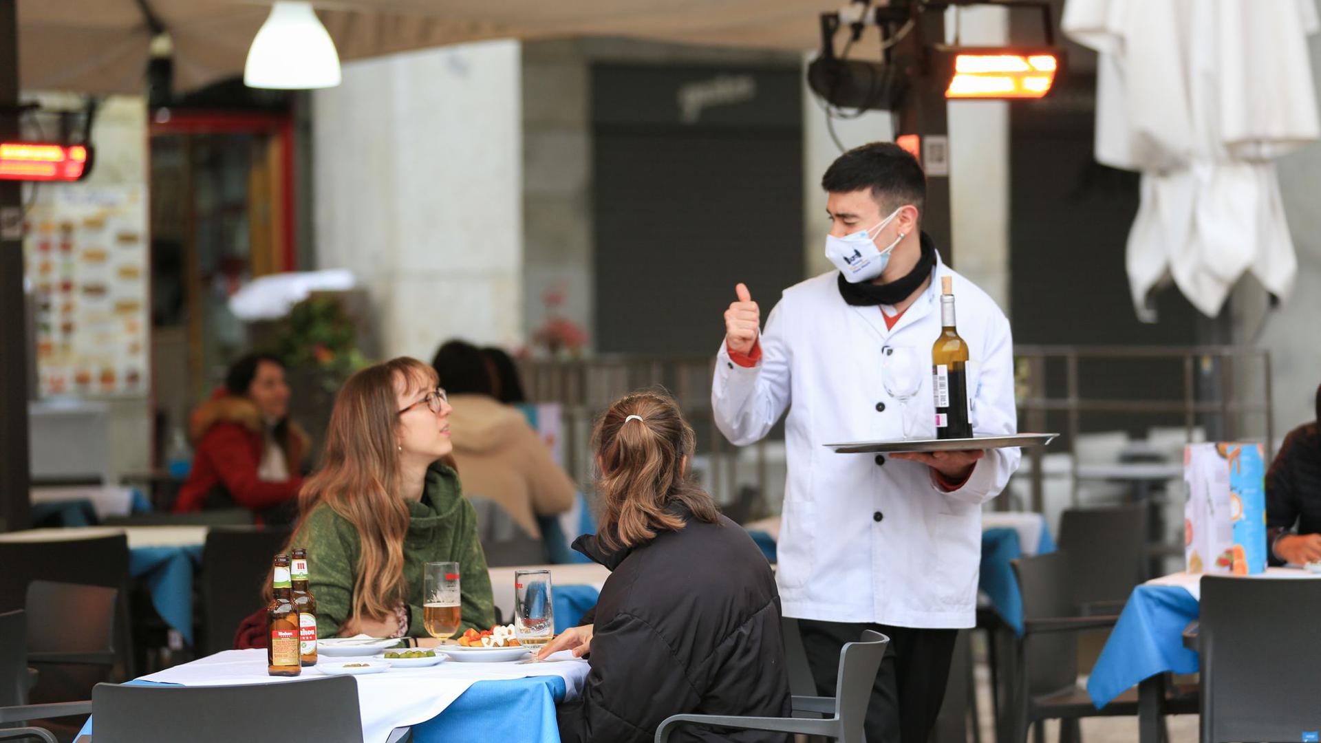 Ein Kellner bedient zwei Kundinnen auf der Terrasse einer Bar im Zentrum von Madrid.