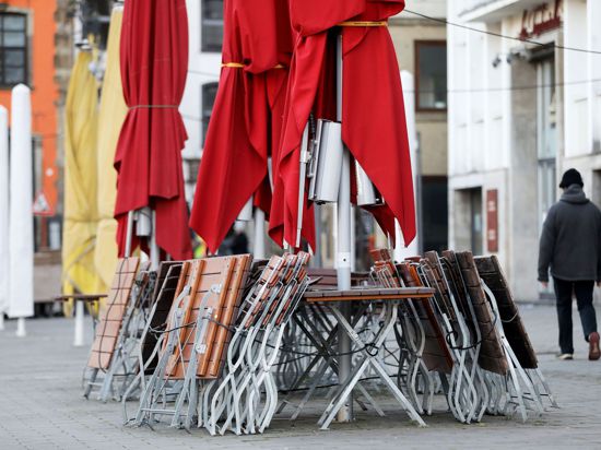 Ein Mann geht auf dem Heumarkt in Köln an zusammengestellten Tischen und Stühlen eines geschlossenen Restaurants vorbei.