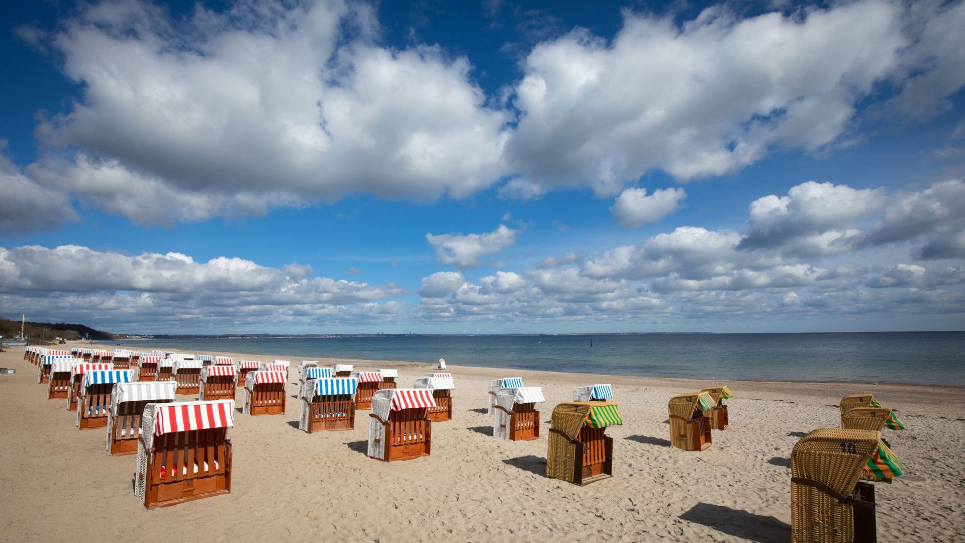 Geschlossene Strandkörbe stehen auf einem fast menschenleeren Strand an der Ostsee.