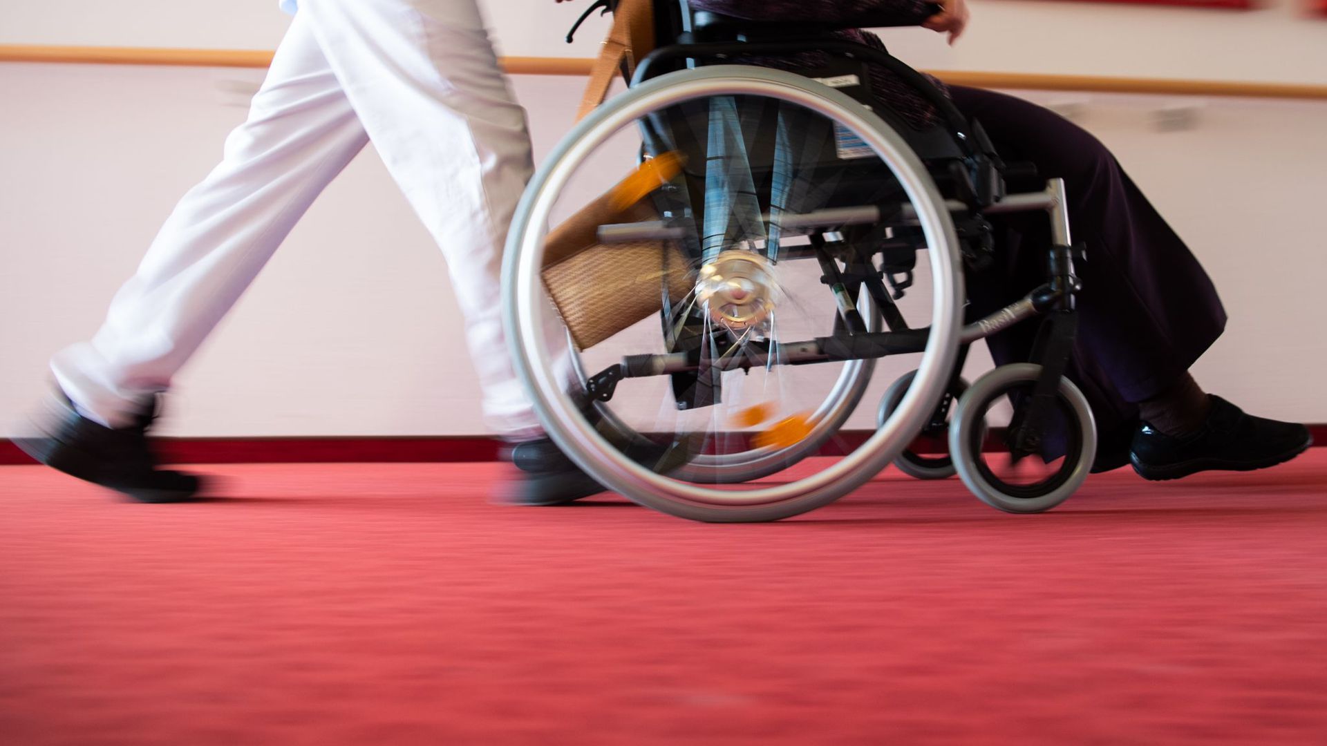 Ein Pfleger schiebt die Bewohnerin eines Pflegeheims in einem Rollstuhl.