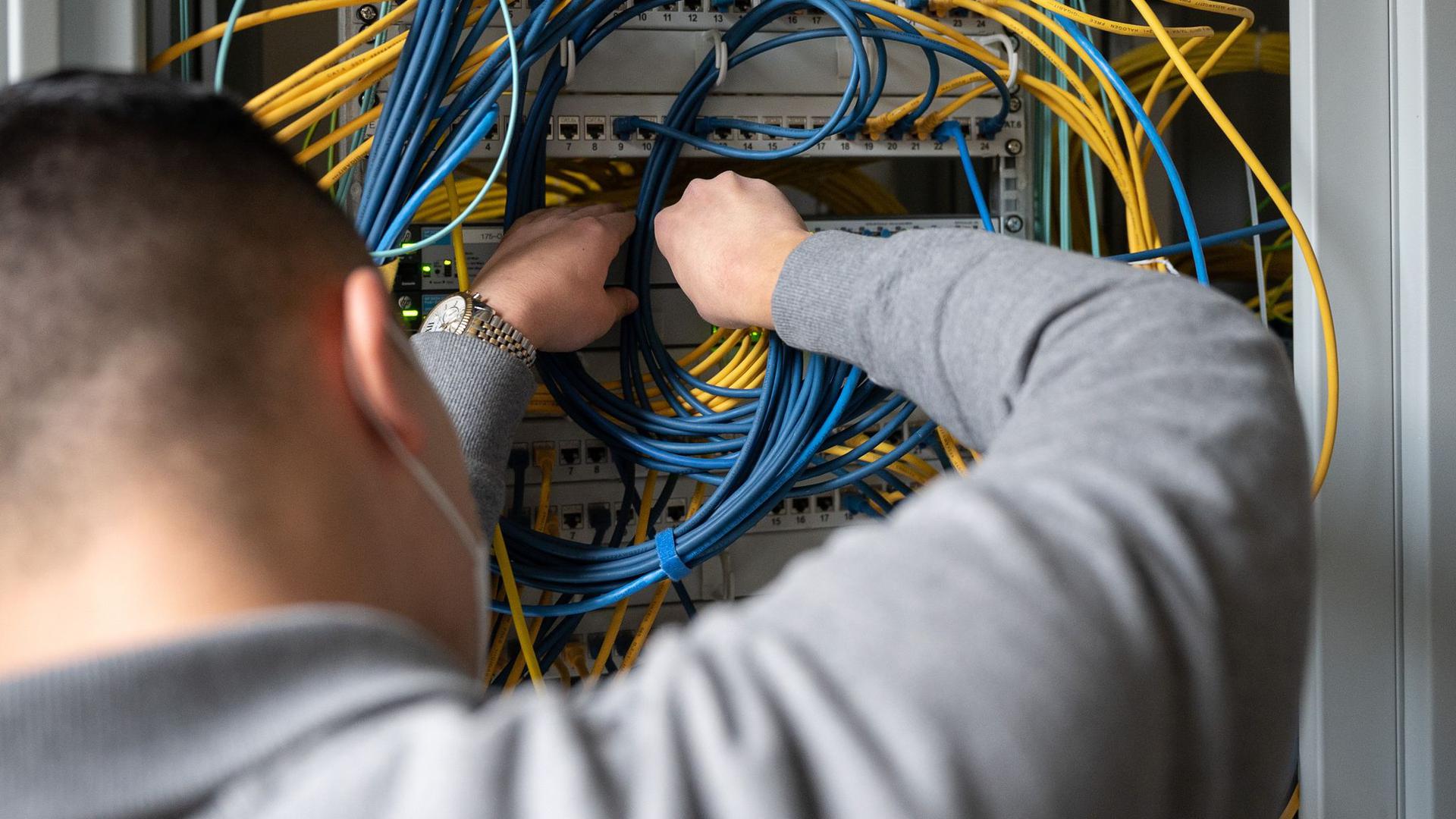 Ein Auszubildender Fachinformatiker Systemintegration bei der IHK Region Stuttgart im 2. Ausbildungsjahr, steckt an einem Server ein Netzwerkkabel ein.