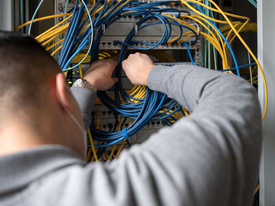 Ein Auszubildender Fachinformatiker Systemintegration bei der IHK Region Stuttgart im 2. Ausbildungsjahr, steckt an einem Server ein Netzwerkkabel ein.