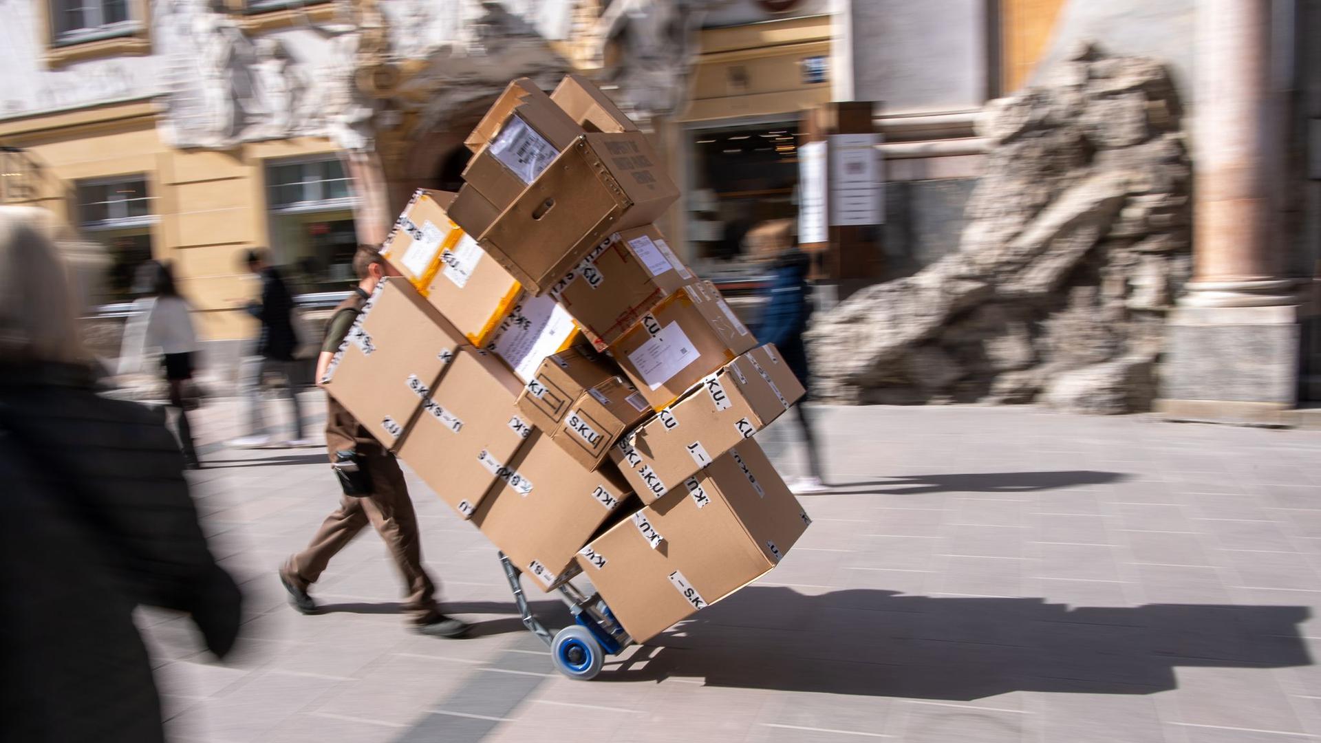 Ein Paketzulieferer transportiert mit einer Sackkarre mehrere Pakete durch die Fußgängerzone.