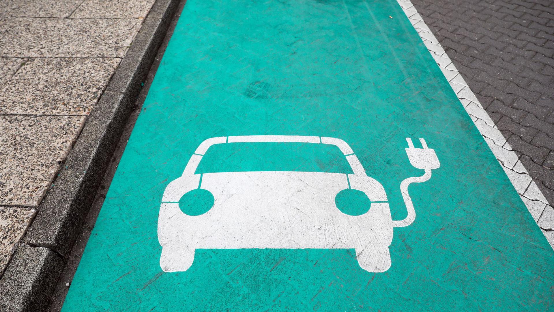 Ein stilisiertes Auto auf grünen Grund markiert einen Parkplatz mit Ladesäule für Elektrofahrzeuge.