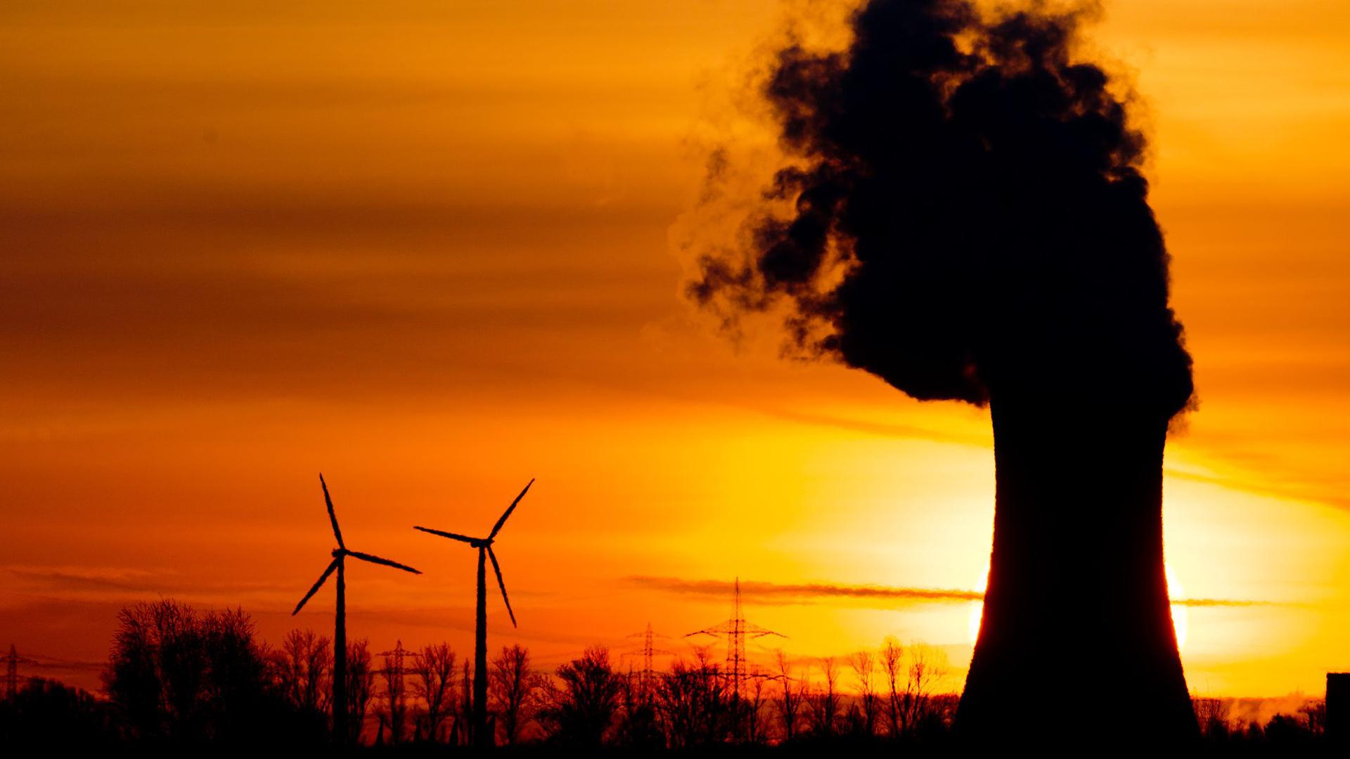 Zwei Windräder und ein Kohlekraftwerk im Licht der aufgehenden Sonne.