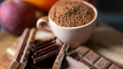 Vollmilchschokolade liegt neben einer mit Kakaopulver gefüllten Tasse auf einem Holzbrett in der Küche. (Archivbild)