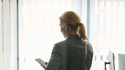 Eine Frau steht in einem Bürozimmer und hält ein Smartphone in der Hand. (Symbolbild)
