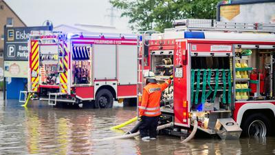 Zwei Einsatzfahrzeuge der niedersächsischen Feuerwehr stehen im Juni 2020 auf dem überschwemmten Parkplatz eines Supermarktes, der wegen Starkregen abgepumpt werden muss.