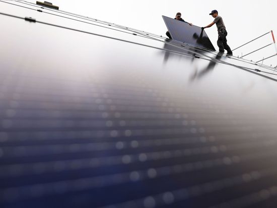 Handwerker montieren auf dem Dach eines Wohnhauses Solarmodule.