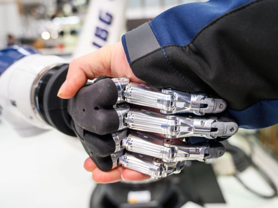 An einem Stand auf einer Messe gibt ein Mann einem Roboter die Hand.