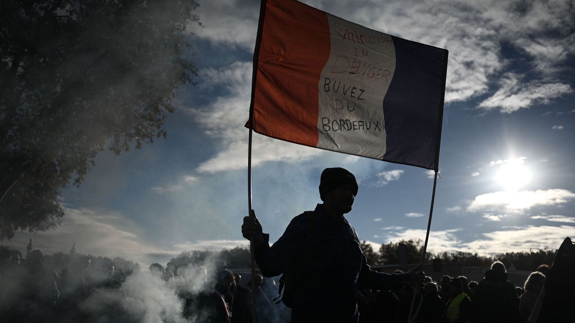 Ein Mann hält eine französische Nationalflagge mit der Aufschrift „Winzer in Gefahr – trinkt Bordeaux-Wein“ hoch.