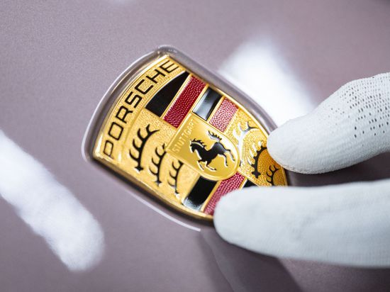Ein Mitarbeiter der Porsche AG zeigt in einer Produktionshalle das Porsche-Logo.