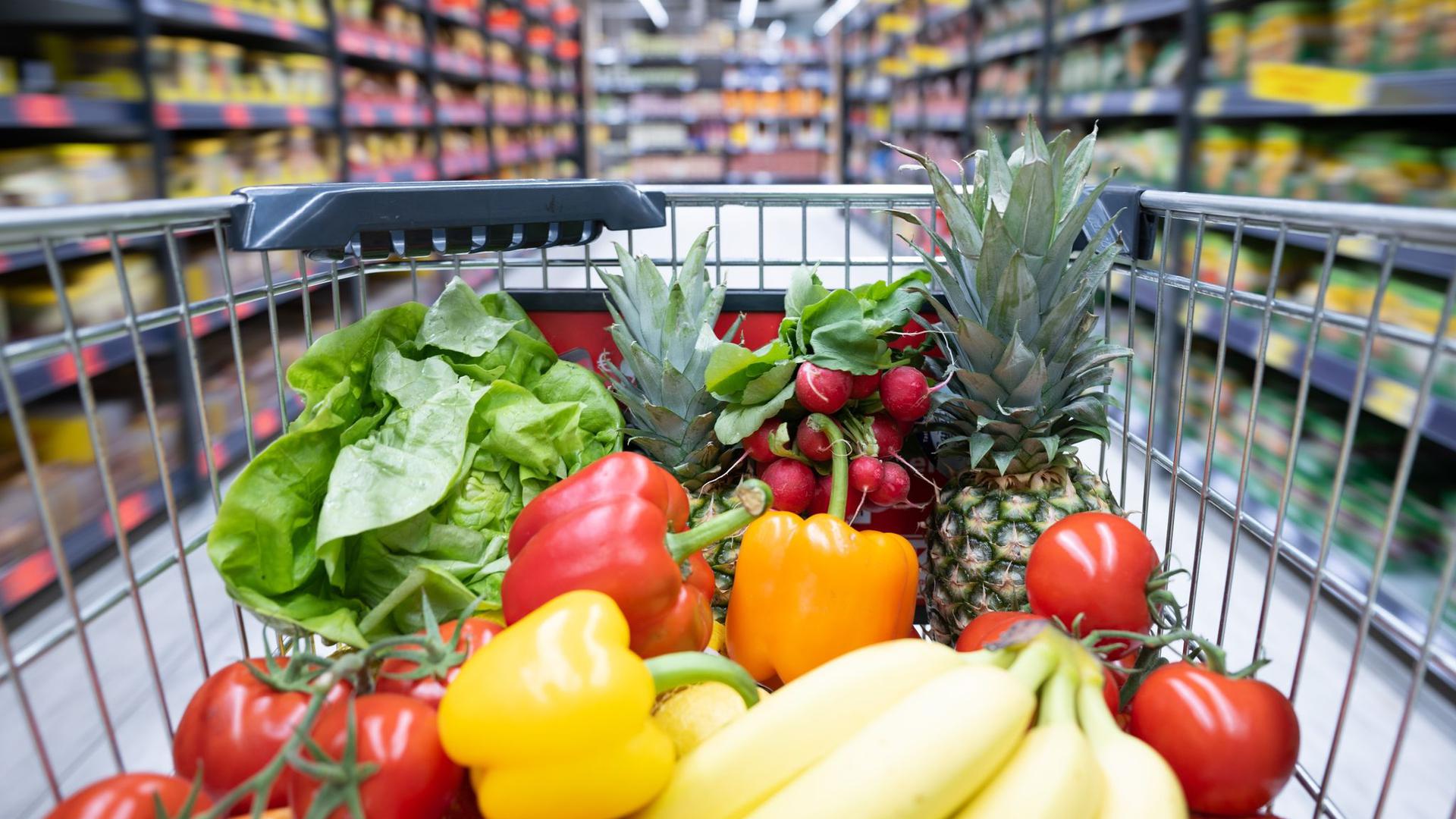 Ein Einkaufswagen voller Gemüse und Obst fährt durch einen Supermarkt.