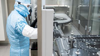 Eine Fachkraft steht an einer Abfüll- und Verschließanlage für pharmazeutische Produkte eines Unternehmens in Singen (Hohentwiel).