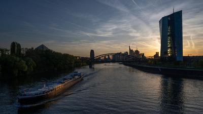 Ein Schiff fährt bei Sonnenuntergang an der EZB in Frankfurt vorbei.