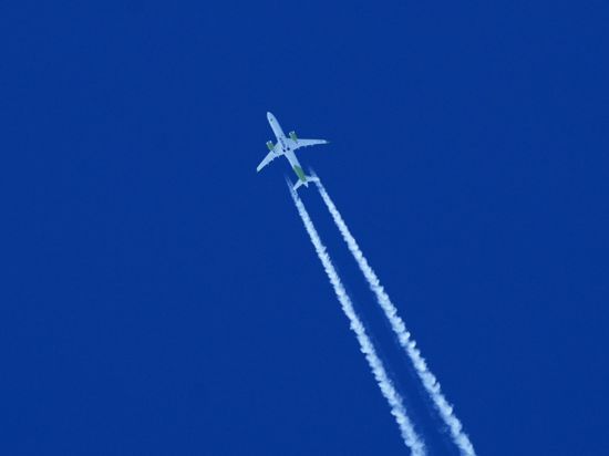 Ein Flugzeug zieht am Himmel einen Kondensstreifen hinter sich her.