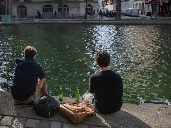 Zwei junge Männer trinken am Ufer des Kanals Saint-Martin in Paris gemeinsam Bier.