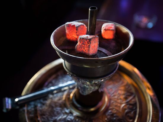 Glühende Kohle liegt auf einem Metallsieb über dem Tabak im Kopf einer Wasserpfeife in einer Shisha-Bar. 