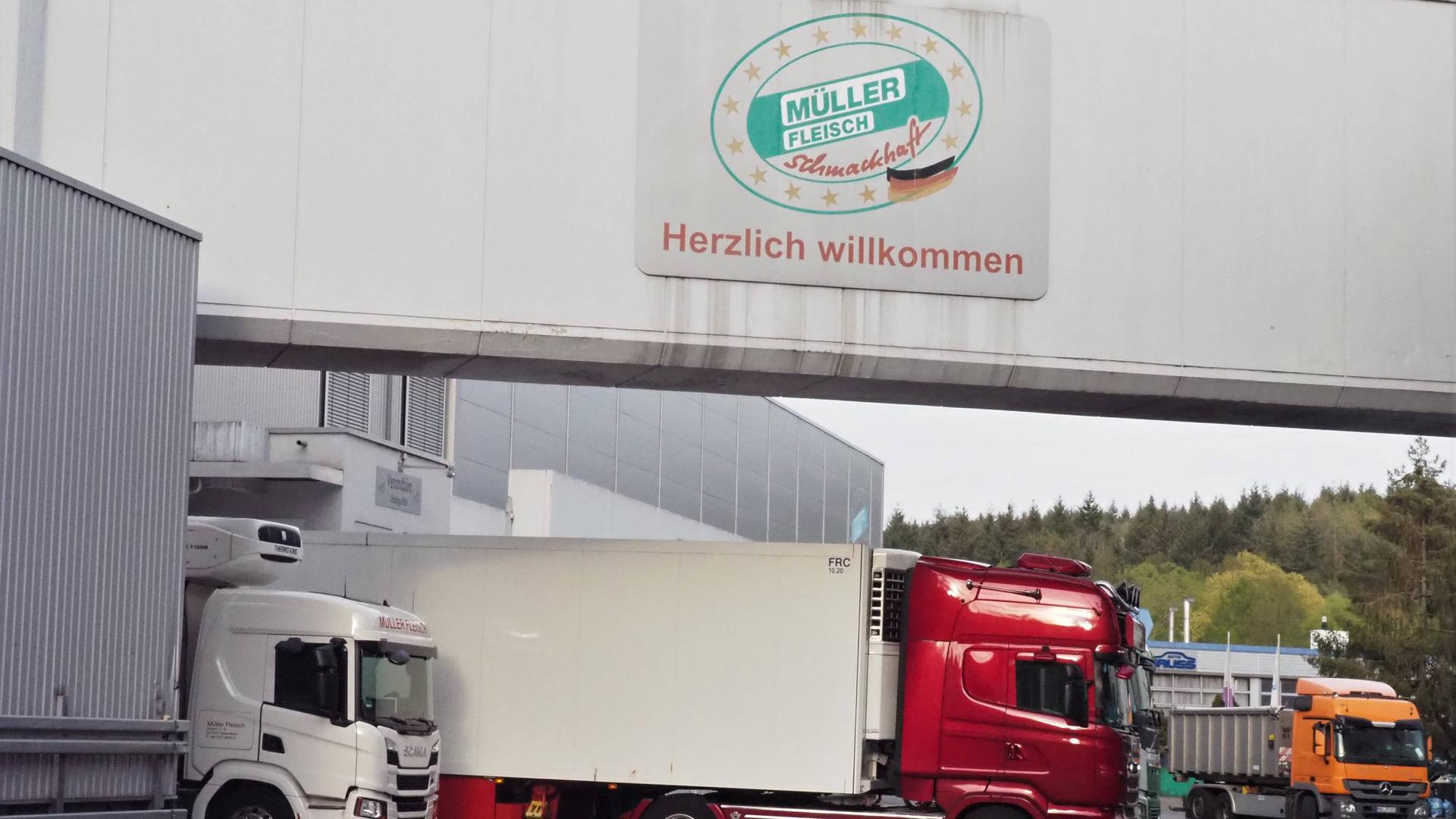 Ein Firmenhof mit mehreren großen Lastwagen an einer Verladerampe. Darüber steht ein Schild an der Halle „Müllerfleisch, herzlich willkommen”. 