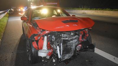 Zerstörtes rotes Auto, dahinter ein Feuerwehrauto.