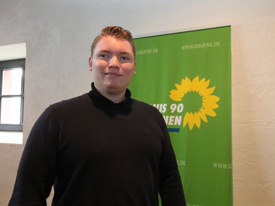 Felix Herkens vor einem Wahlplakat der Grünen mit Sonnenblumen. 