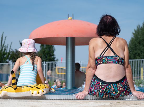 Eine Frau und ein Kind sitzen am Rand eines Schwimmbeckens.